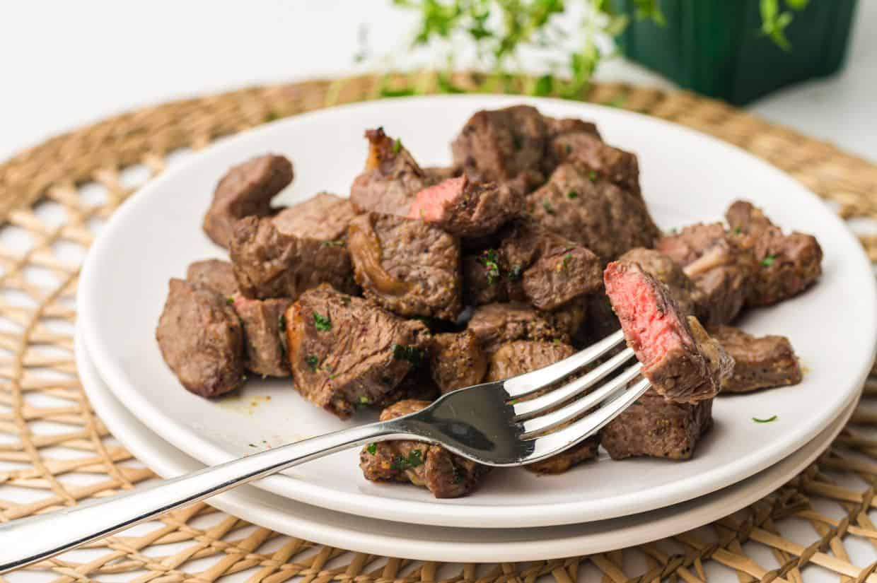 A plate of juicy, seasoned steak bites cooked in an air fryer, garnished with chopped herbs.