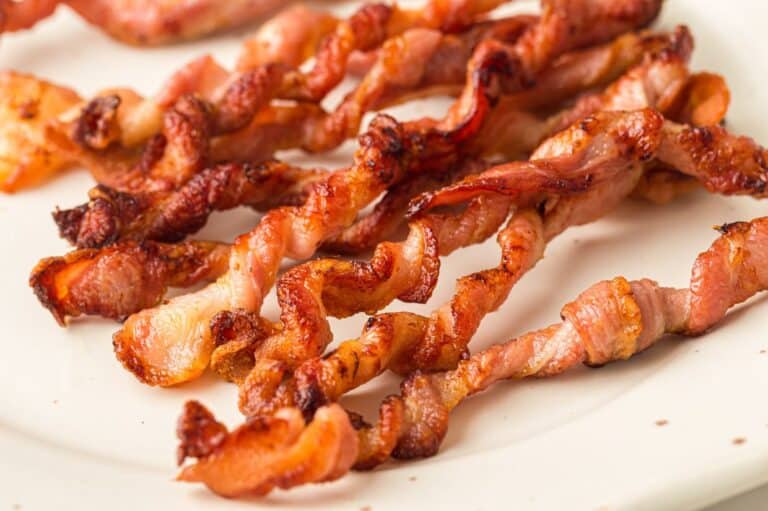 Close-up of crispy, twisted bacon strips served on a white plate, showcasing their golden-brown texture.