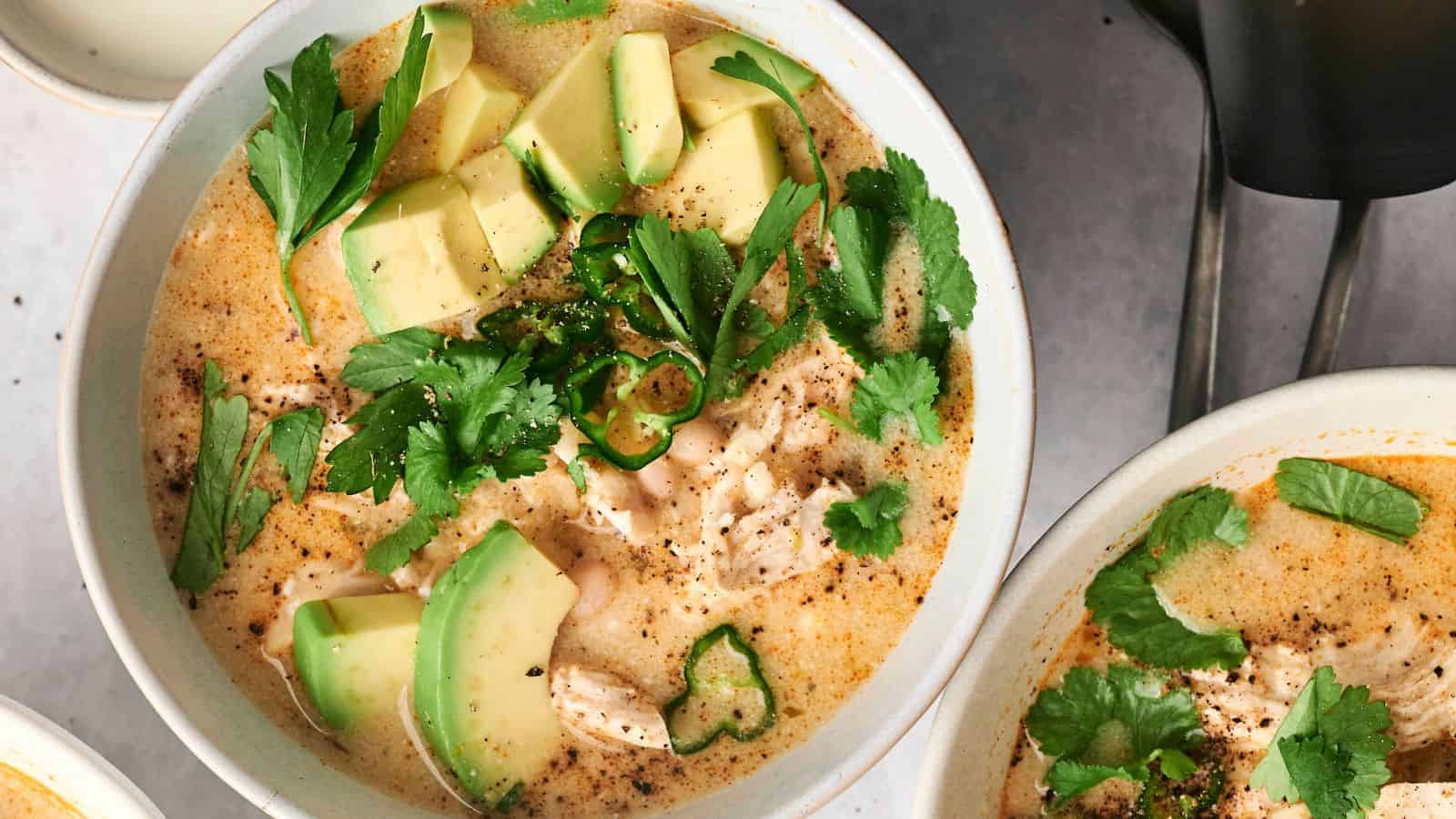 A bowl of creamy air fryer white chicken chili, topped with avocado slices, cilantro, and sliced chili peppers.