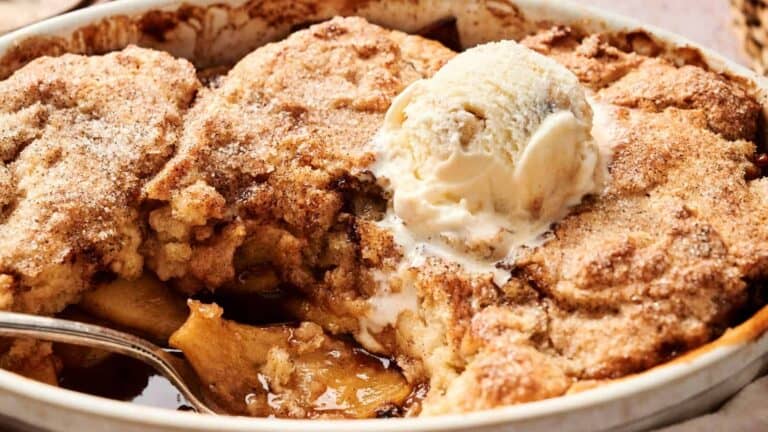 A baked apple cobbler with a scoop of vanilla ice cream on top, partially served in a dish.