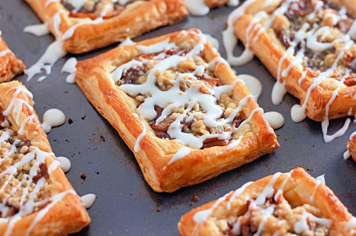 A close-up view of rectangular apple crumb danishes made with golden-brown puff pastry, drizzled with white icing and topped with a crumbly streusel.