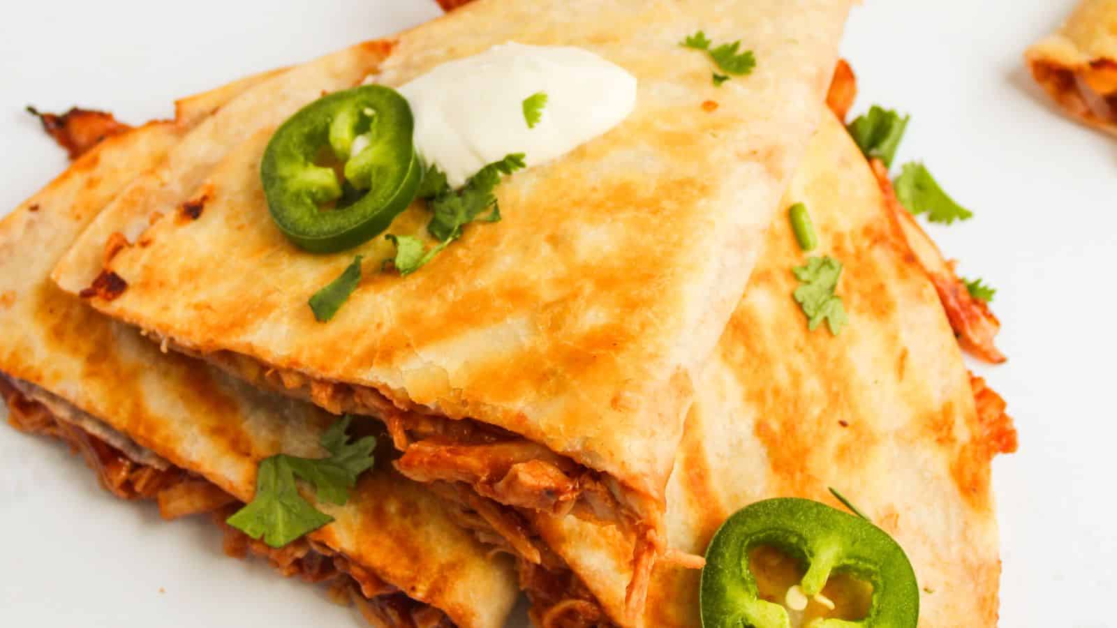 Quesadillas stacked on a plate, topped with sliced jalapeños, cilantro, and a dollop of sour cream.