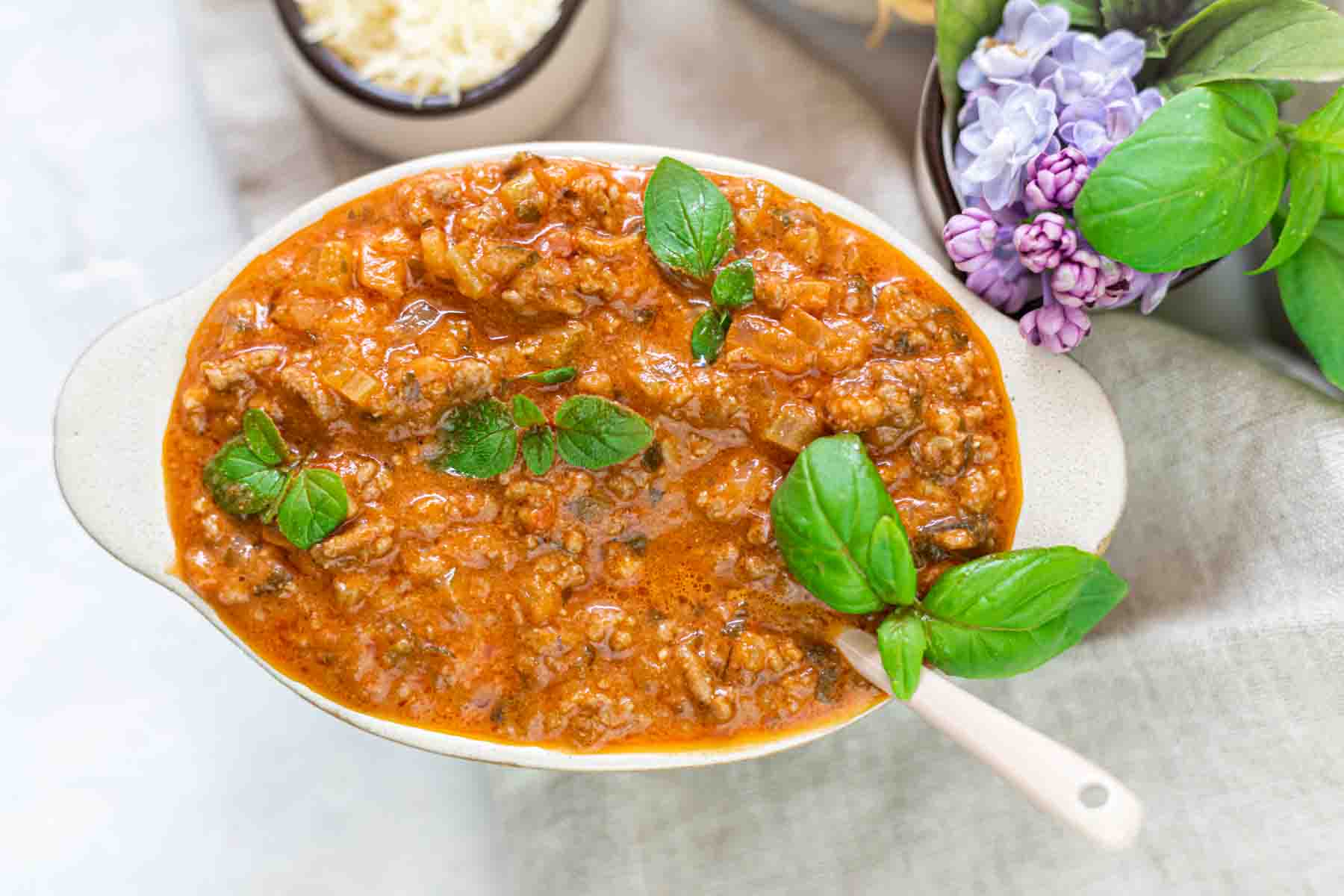 A bowl of beef bolognese gravy garnished with fresh basil.