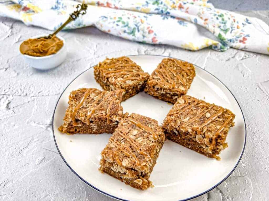 A white plate with five biscoff cookie butter streusel bars, each drizzled with melted cookie butter.