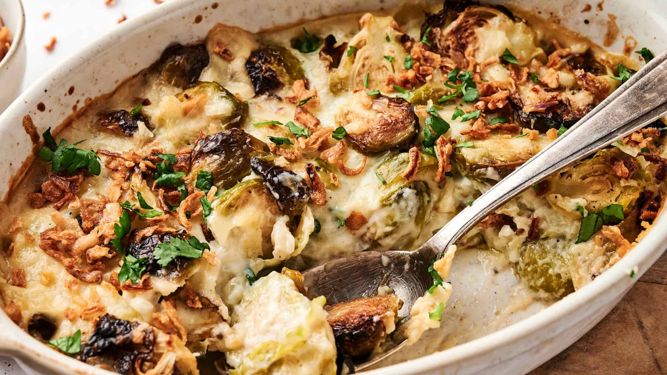 Casserole dish with Brussels sprouts, crispy onions, cheese, and herbs, mixed with a spoon.