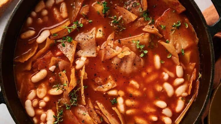 A close-up of a steaming pot of hearty cabbage soup in a tomato-based broth, garnished with fresh herbs.