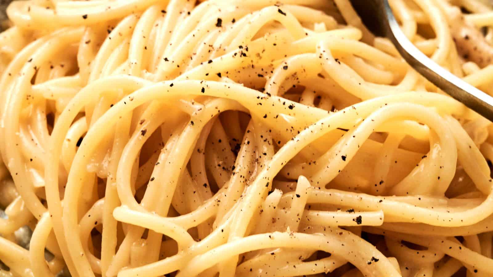 Close-up of cooked spaghetti with cracked black pepper and a fork partially visible.