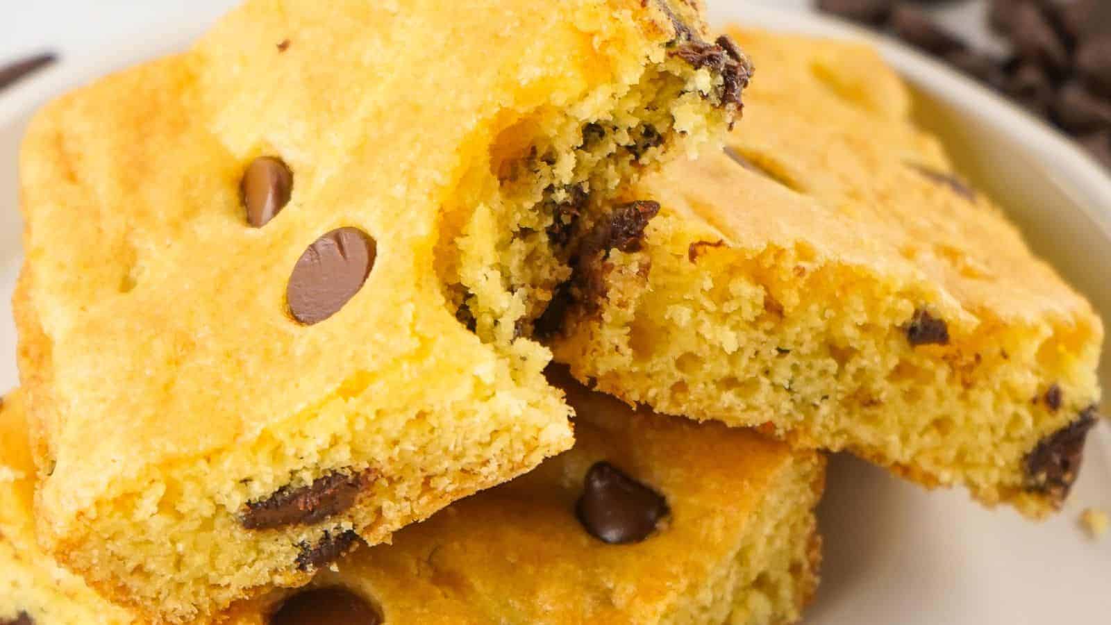 Close-up of three stacked blondies with chocolate chips, resembling cake mix chocolate chip cookie bars, one of which has a bite taken out of it.