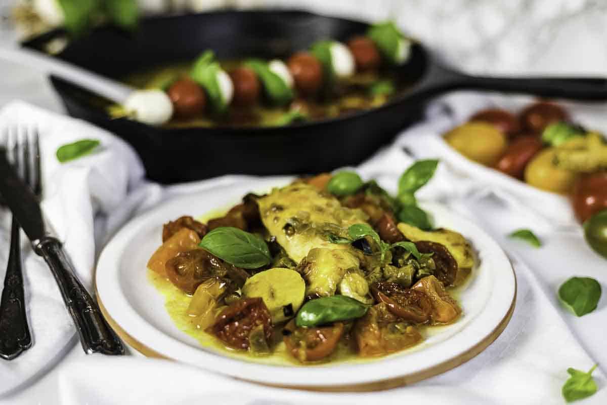 Caprese Chicken served on a plate with fresh basil, surrounded by vibrant ingredients and a skillet in the background.