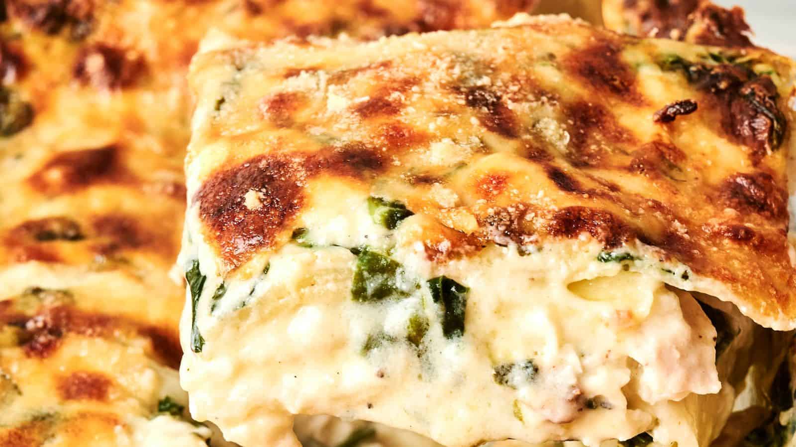 Close-up of a slice of creamy lasagna with browned cheese on top and visible layers of pasta, spinach, and sauce.