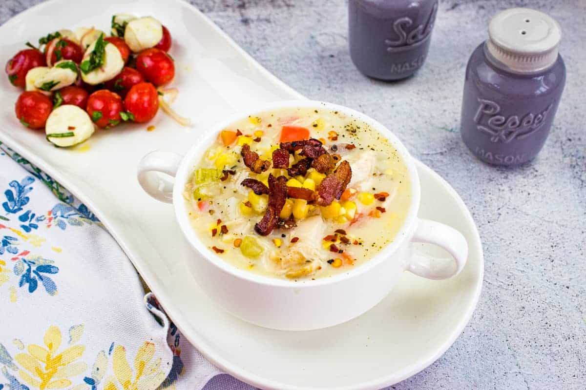 A bowl of chicken and corn chowder topped with bacon, served with a tomato and mozzarella salad.