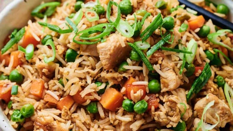 Close-up of chicken fried rice with peas, carrots, sliced green onions, and chopsticks.