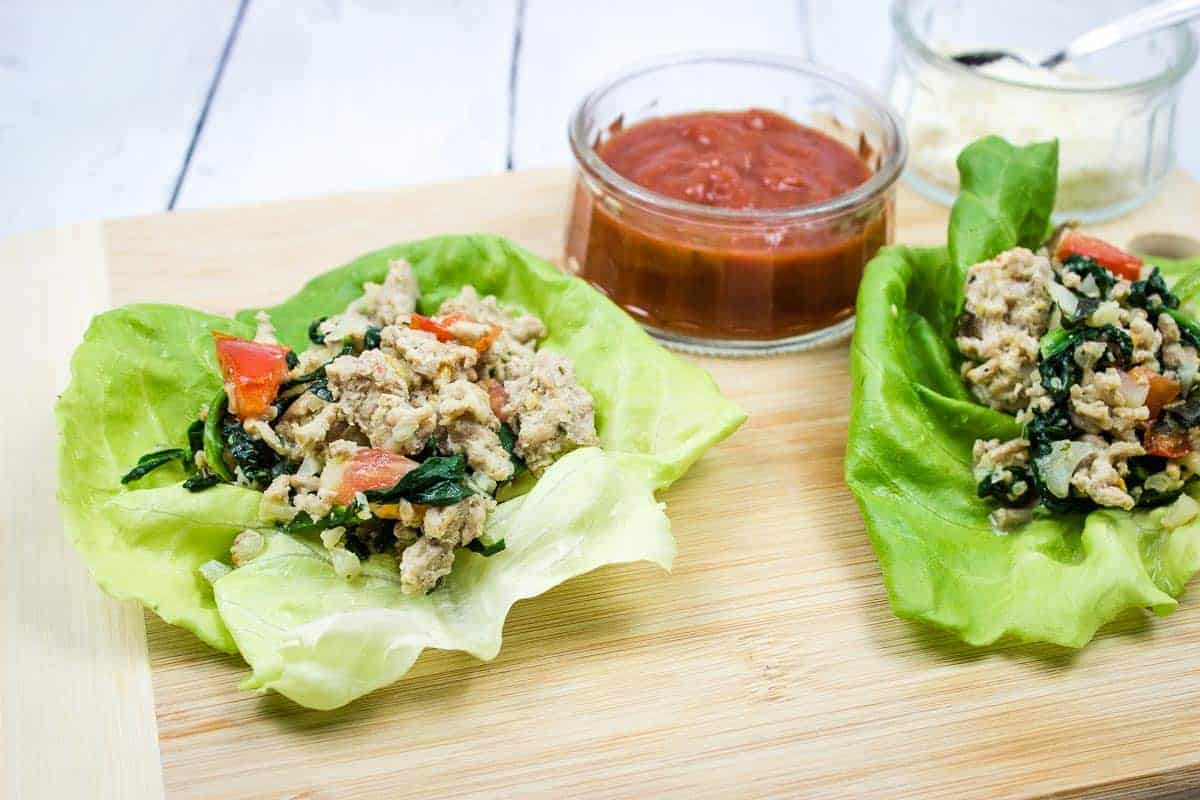 Two chicken parmesan lettuce wraps on a cutting board.