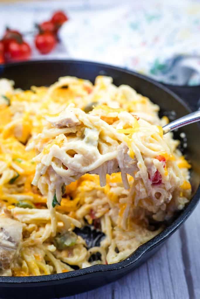 A close-up image of creamy chicken spaghetti being lifted with a spoon from a black skillet.