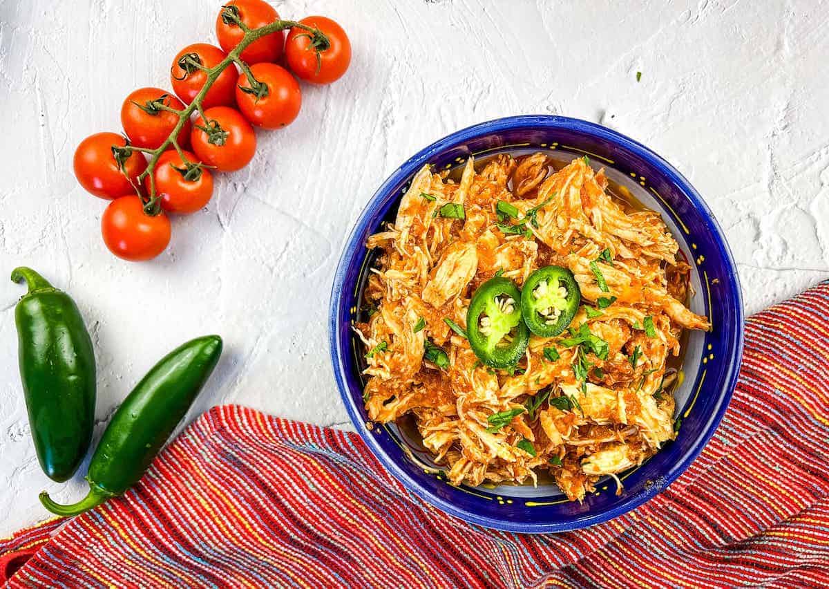 Chicken tinga in a blue bowl with cherry tomatoes and green peppers on the side.