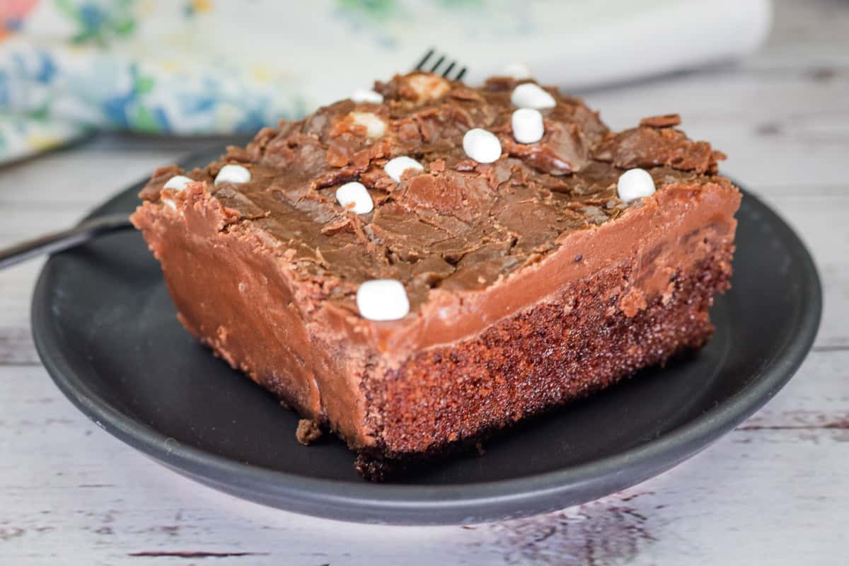 A slice of Grandma's Coca-Cola cake with chocolate frosting and small marshmallows on a black plate.