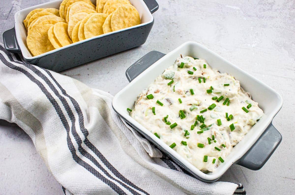 A bowl of cold crab dip with crackers and chives.