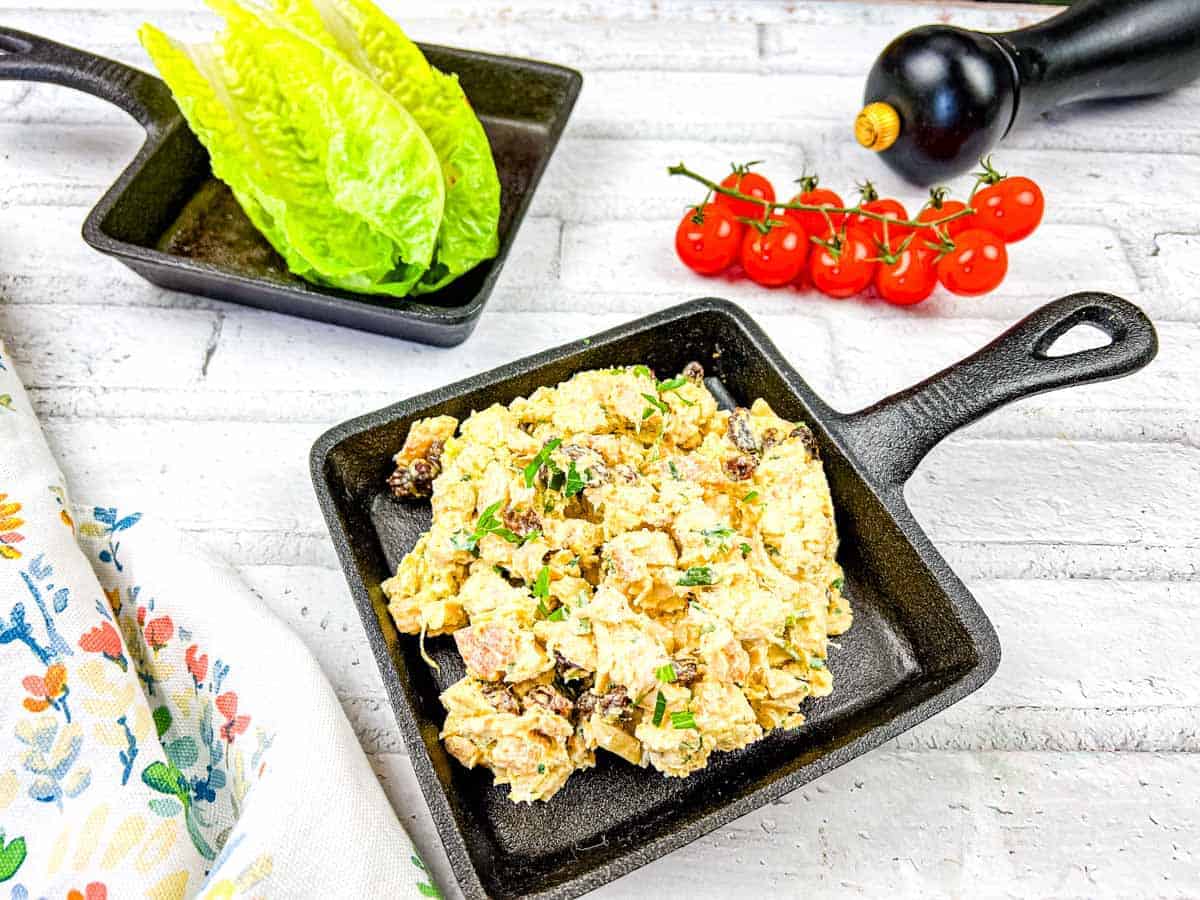 A serving of coronation chicken salad beside a croissant filled with salad, accompanied by cherry tomatoes, all on the same plate.