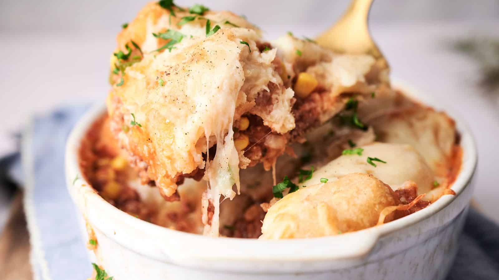 Close-up of a cowboy casserole in a white dish, showing layers of ground meat and vegetables topped with a golden-brown mashed potato crust, garnished with chopped parsley.