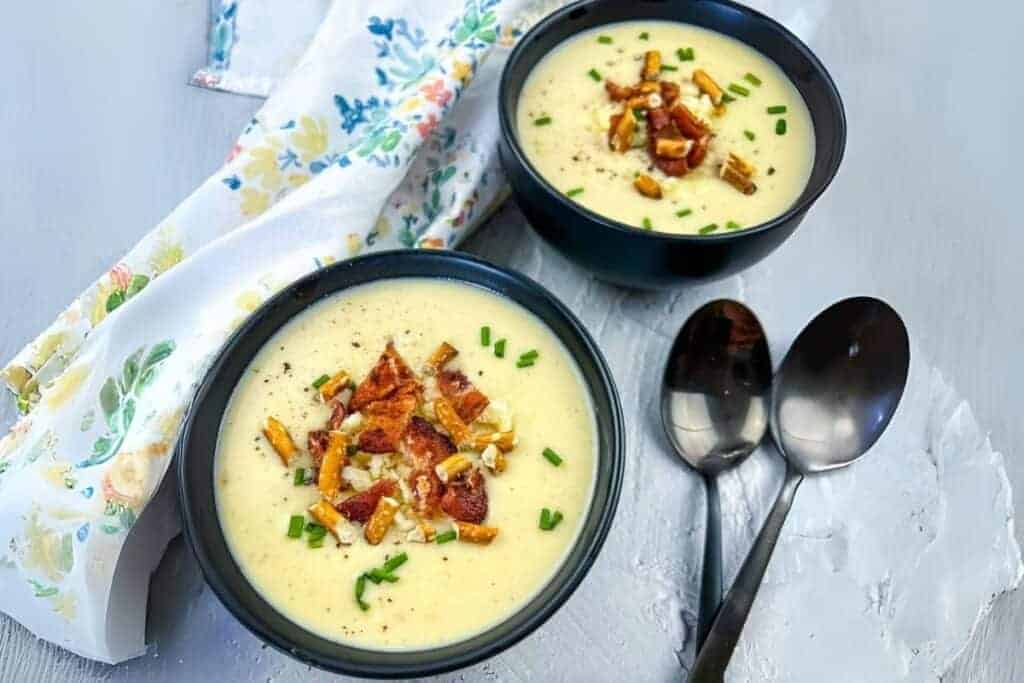 Two bowls of Creamy Potato-Bacon-Cheddar Soup topped with crispy bacon bits and chopped chives.