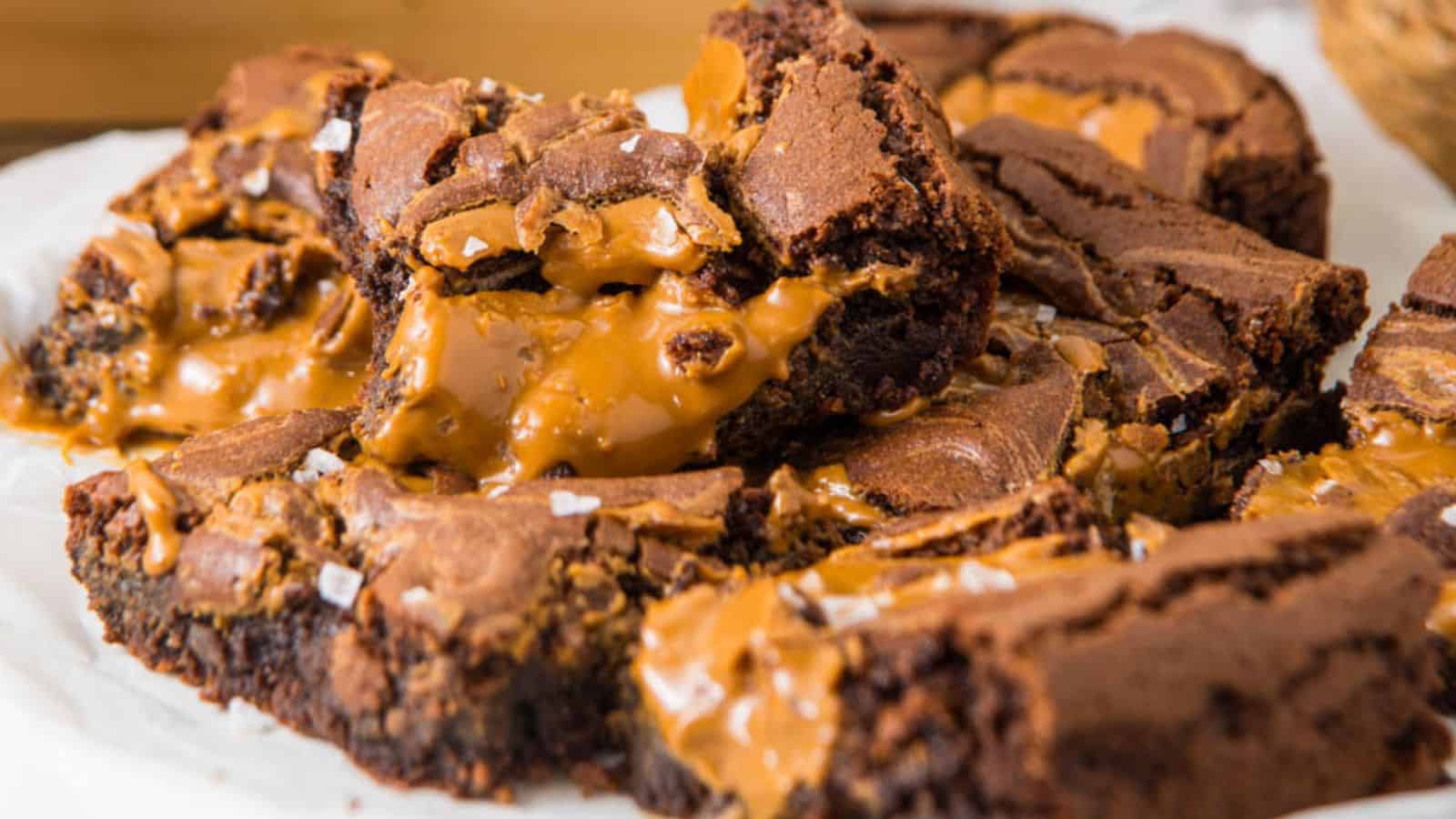 Close-up of a stack of gooey caramel-filled Biscoff Brownies, sprinkled with flaky sea salt, on parchment paper.