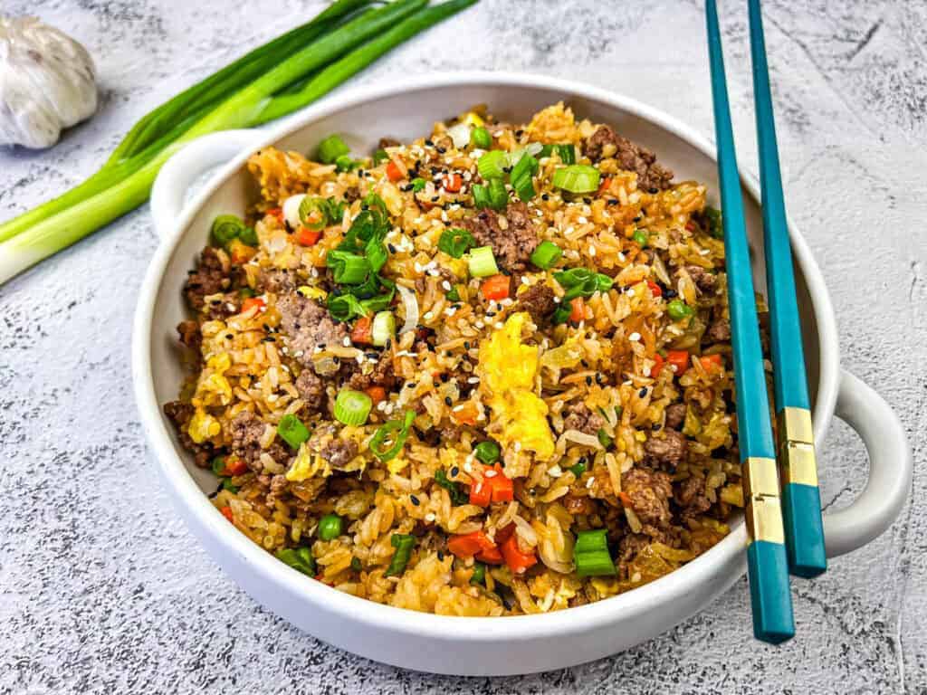 Ground Beef Fried Rice served in a white bowl with blue chopstick on top.