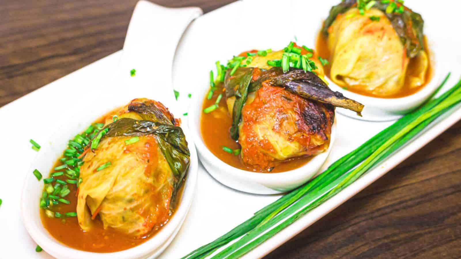 Three serving of cabbage rolls with sauce on a white plate.