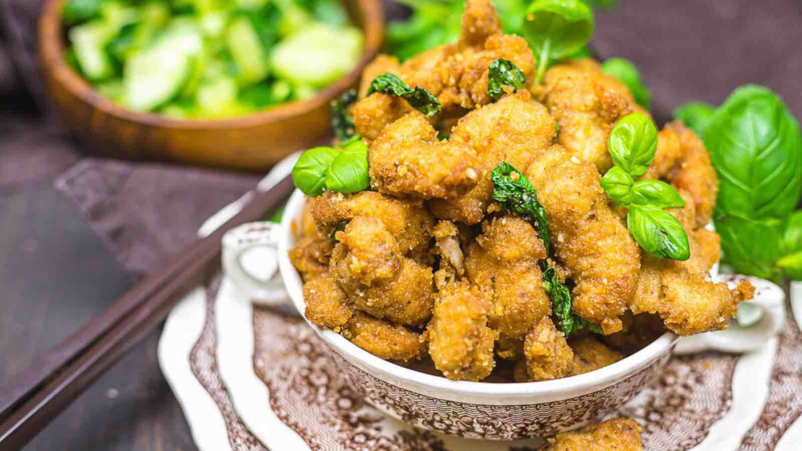 A bowl of crispy fried chicken garnished with basil leaves.