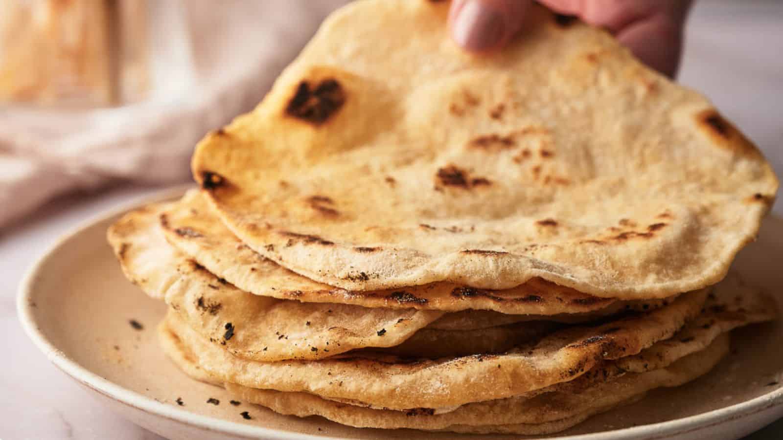 Someone placing a tortilla on a stack of tortillas.