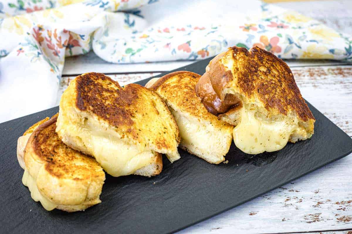 Four garlic bread grilled cheese sandwich halves on a black slate plate.