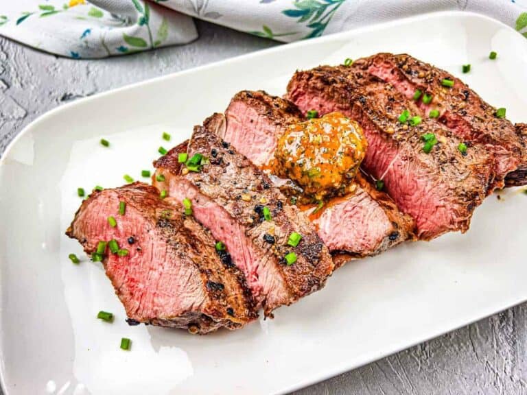 A grilled steak with cowboy butter on a white plate.