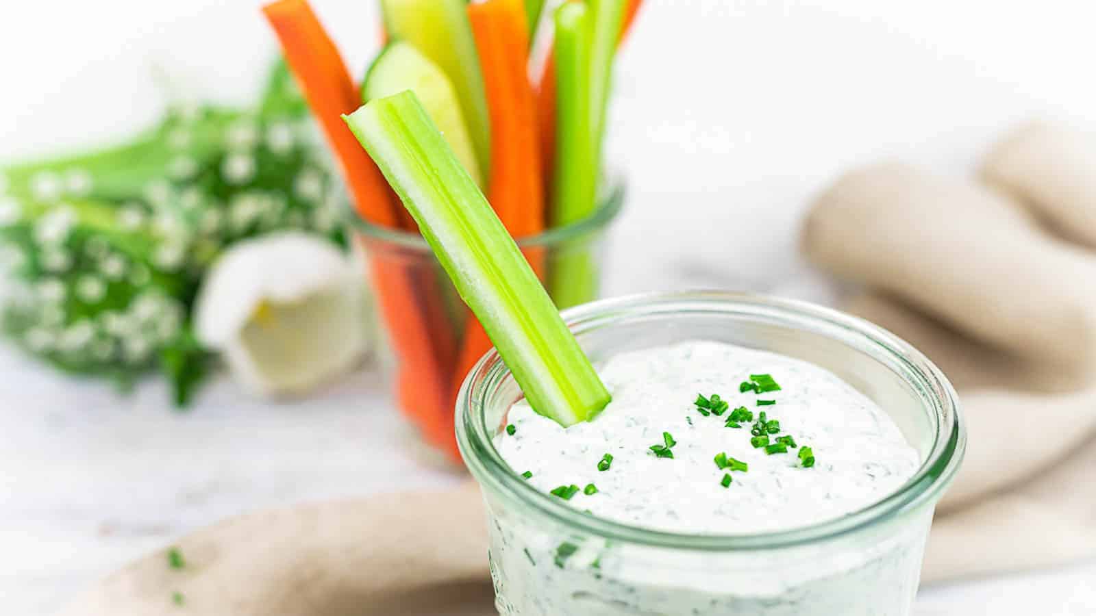 Ranch dressing in a glass bowl with a stick of veggie.