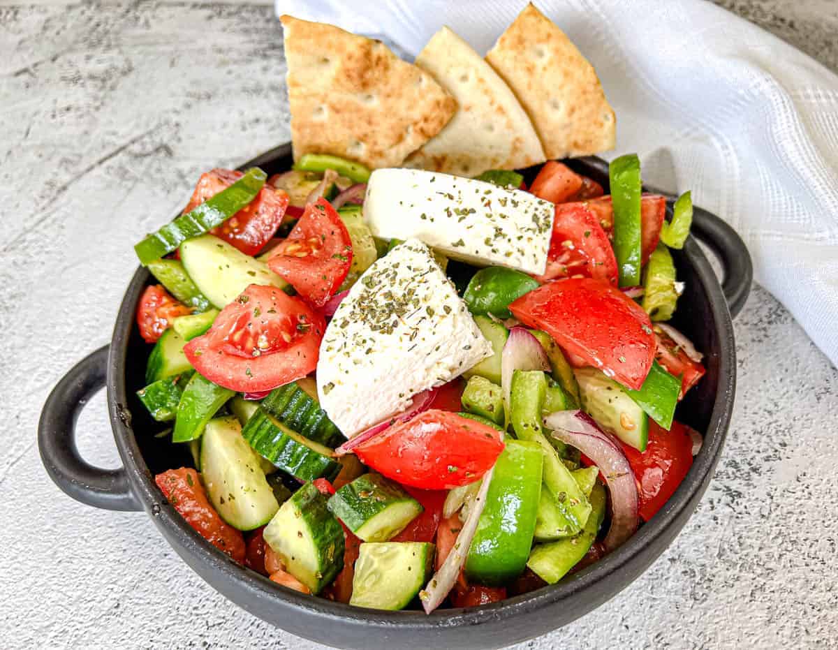 Horiatiki Salad with feta cheese on top served on a plate.