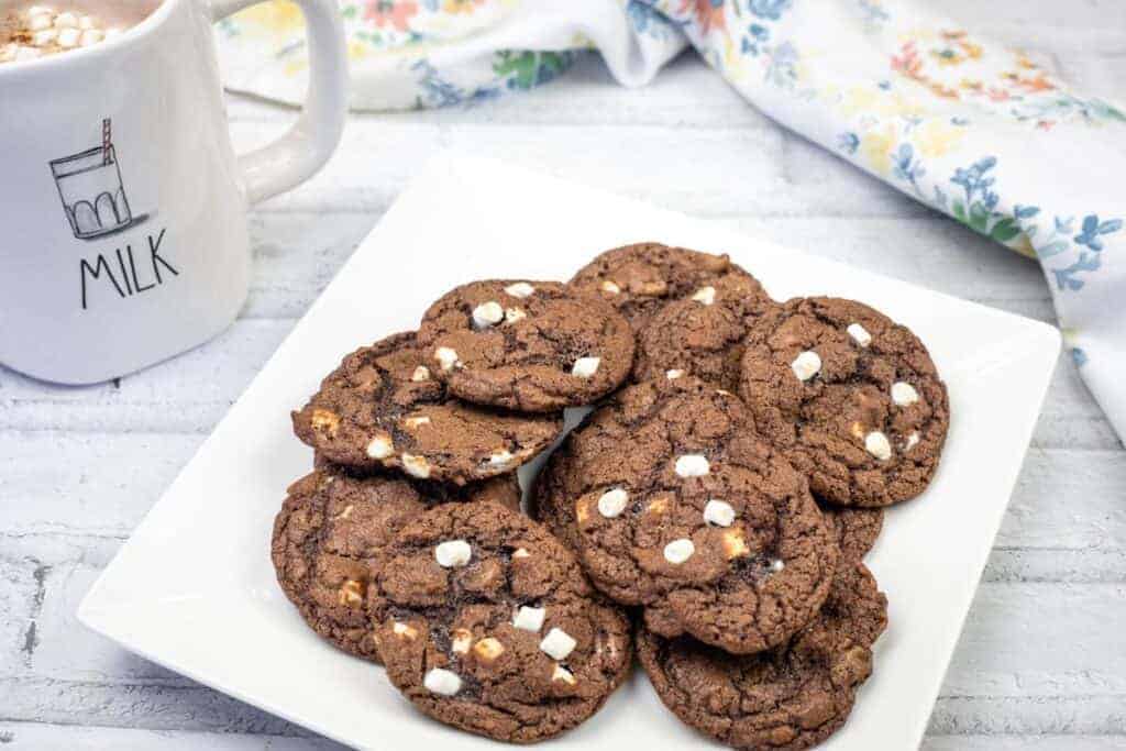 A white square plate with a stack of chocolate cookies featuring white chocolate chips.