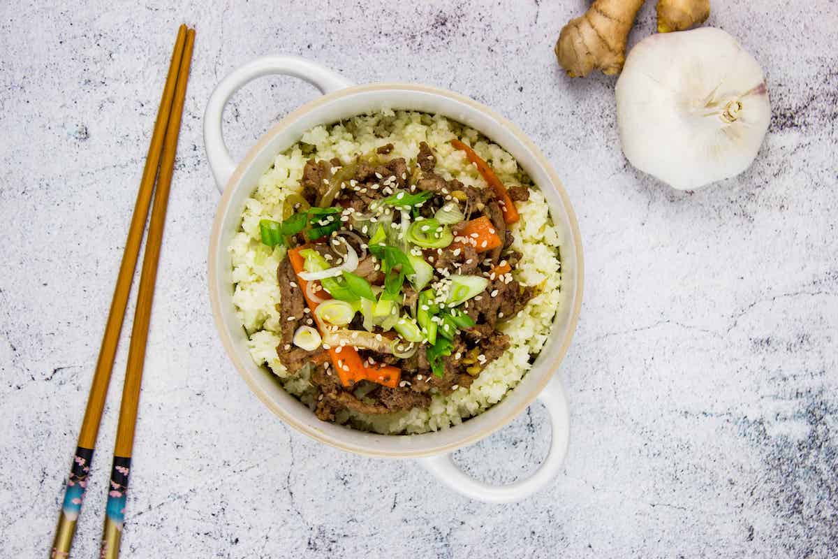 A top-down shot of Korean Beef Bowl with chopsticks, garlic, and ginger on the side.