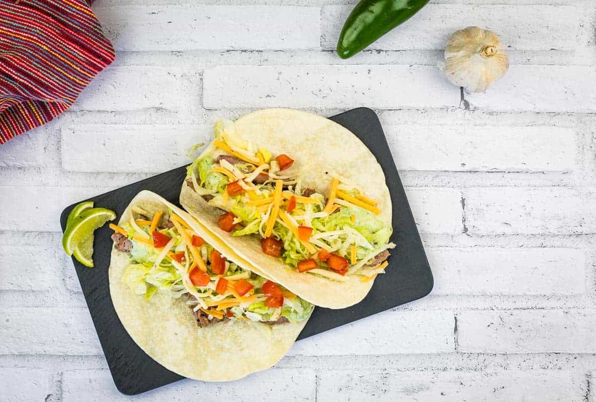 Top-down shot of two Leftover Steak Soft Tacos on a slate board.