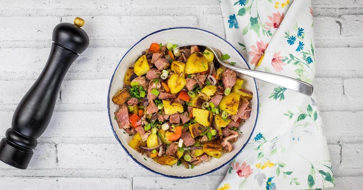 A bowl of leftover cottage roll hash on a white tablecloth.