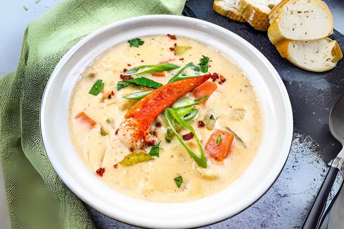 A bowl of creamy lobster chowder garnished with sliced green onions and herbs.