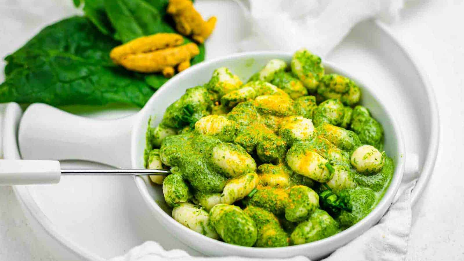 Bright green gnocchi sauce with orange turmeric powder over the gnocchi plate.