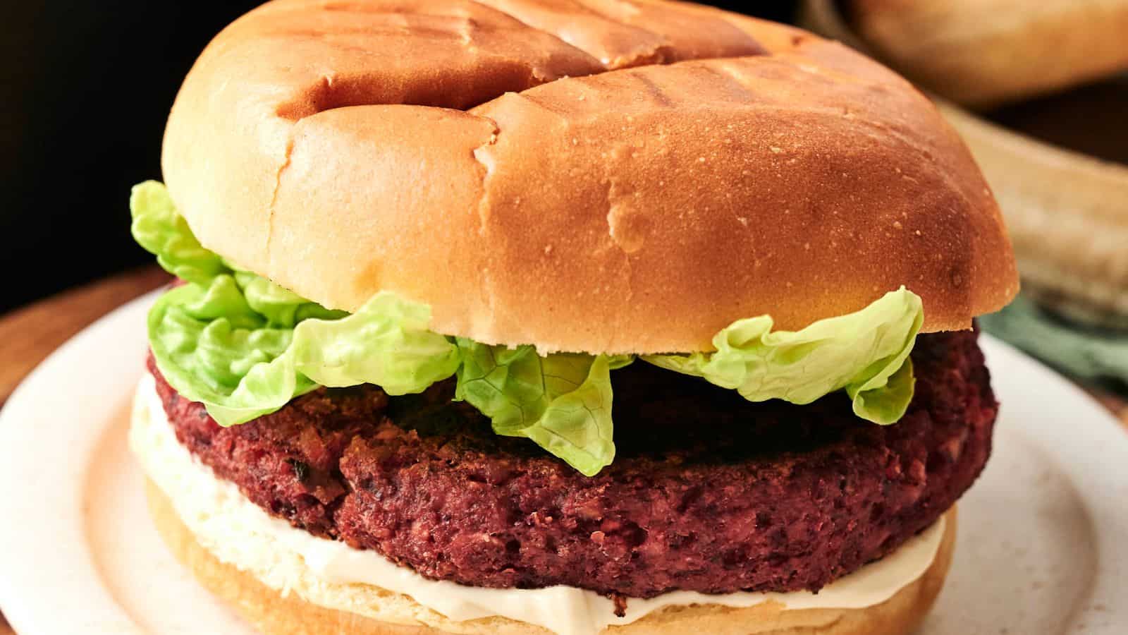 Close-up of a burger with a plant-based patty, lettuce, and sauce in a bun.