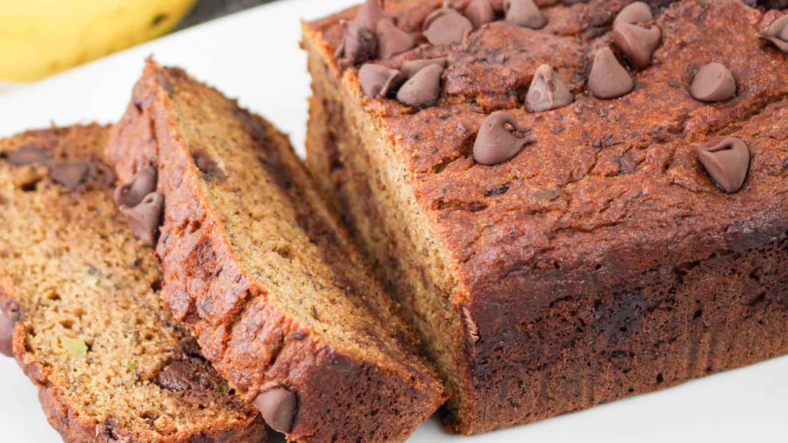 Sliced loaf of chocolate chip banana avocado bread on a white surface. The bread has a golden-brown crust with chocolate chips on top and visible throughout the slices.