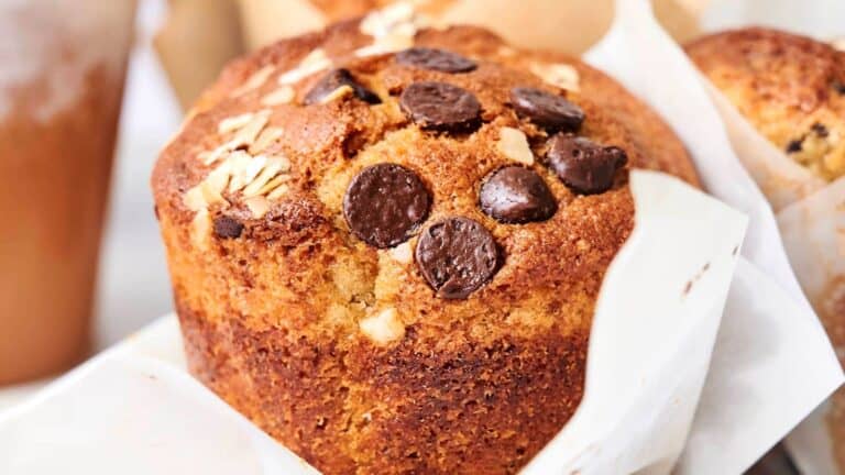 Moist Banana Chocolate Chip Muffins topped with chocolate chips and oats, wrapped in a paper liner.