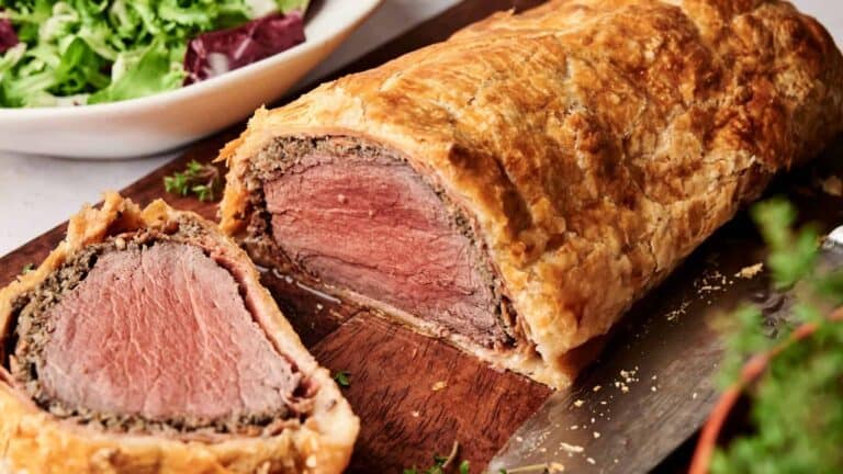 Beef Wellington sliced on a wooden board with a side salad in the background.