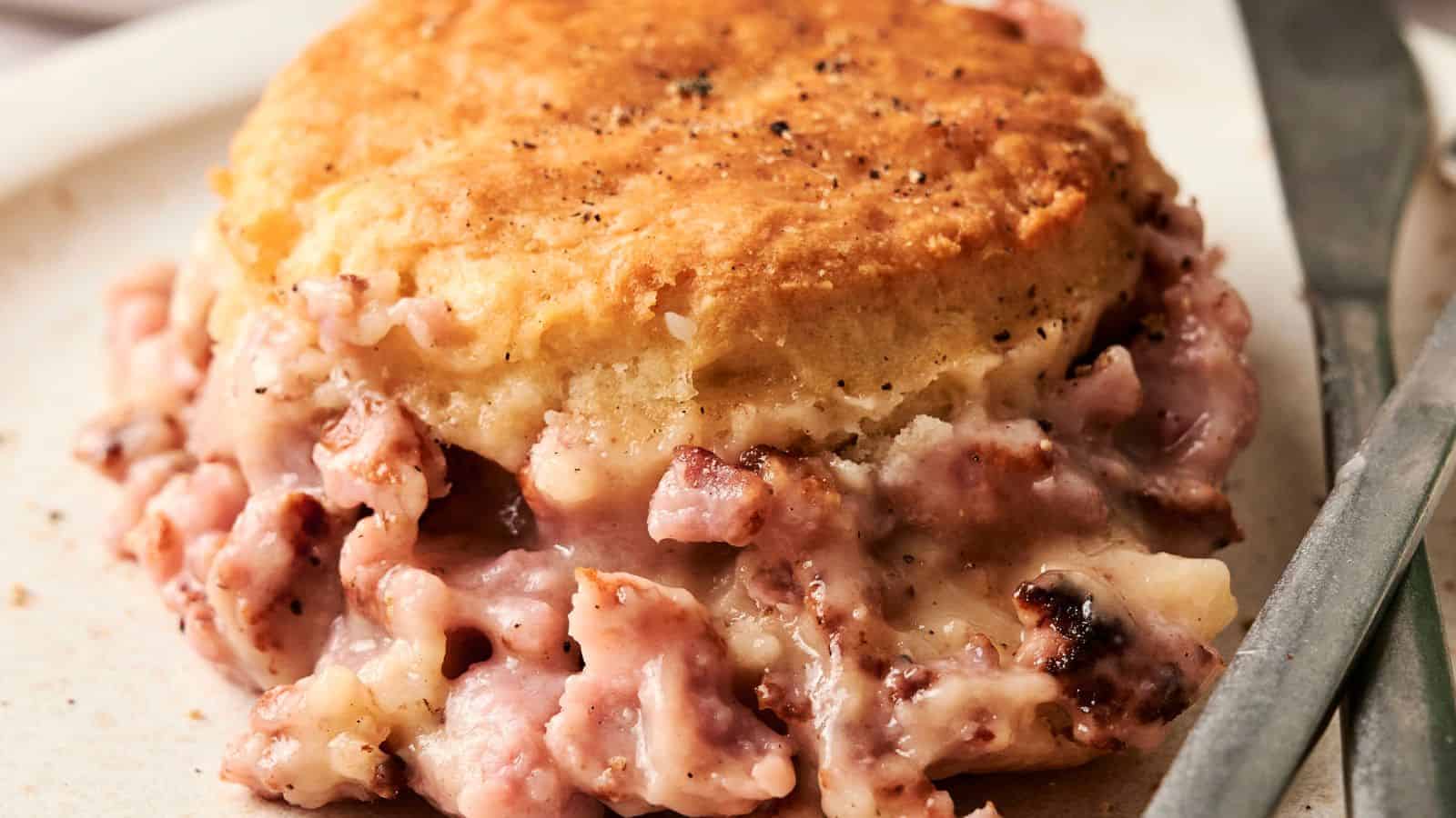 Close-up of a savory biscuit with a creamy ham filling, looking like a gourmet twist on a Biscuits and Gravy Casserole, served elegantly on a plate.