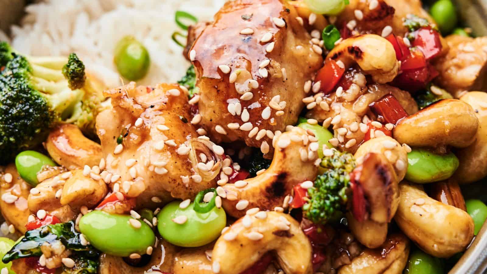 Close-up of Cashew Chicken featuring tender chicken, broccoli, edamame, cashews, and red bell peppers. This delightful dish is topped with sesame seeds and served over a bed of rice.