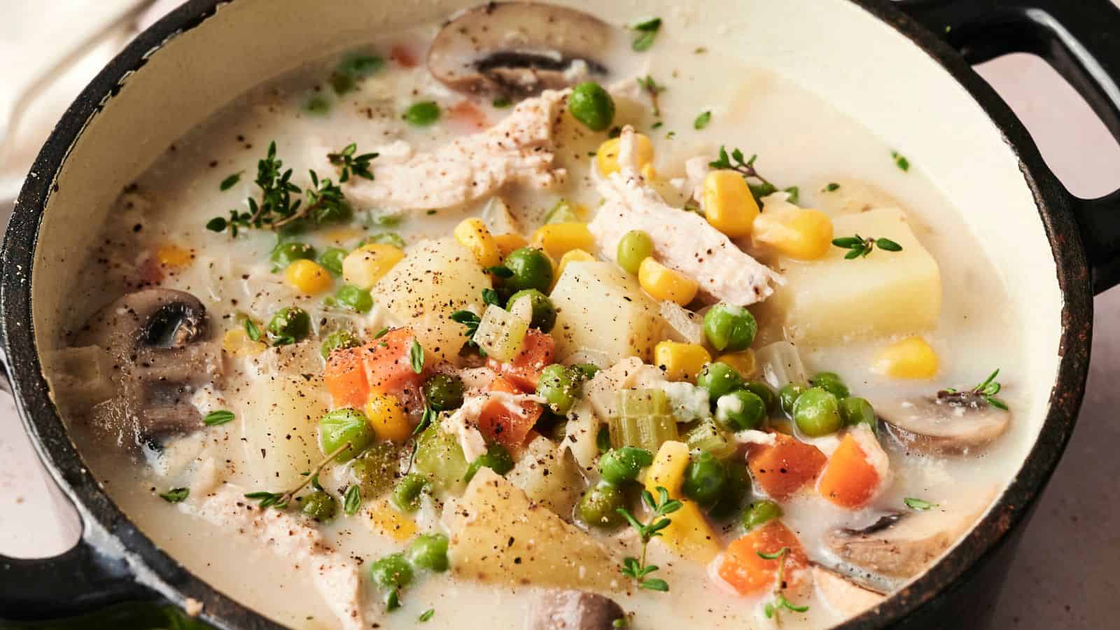 A pot of creamy vegetable and chicken soup with mushrooms, corn, peas, carrots, and herbs.