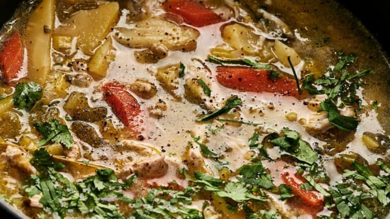 Close-up of a hearty chicken soup with sliced carrots, potatoes, and sprinkled herbs in a broth.