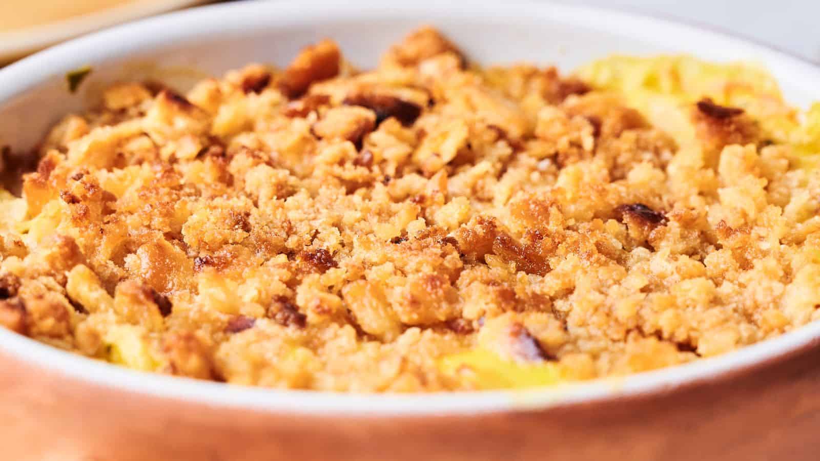 Close-up of a baked apple crumble dessert in a ceramic dish, featuring a golden-brown crumbly topping.