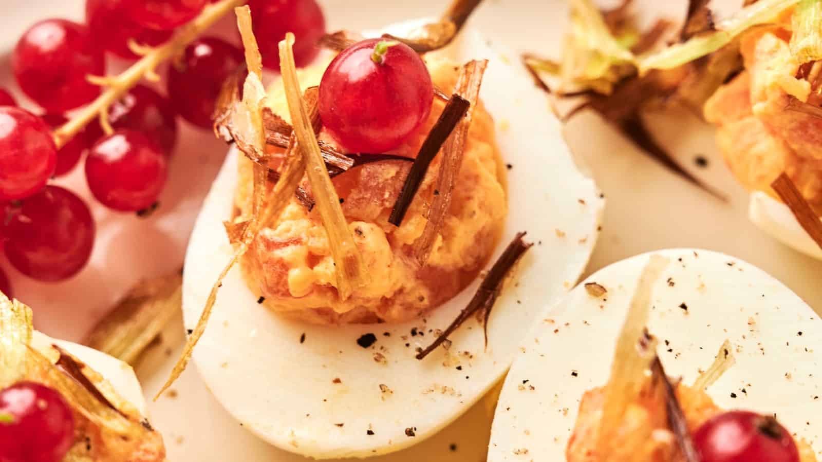 Close-up of Deviled Eggs topped with a red currant and garnished with fried leeks. Fresh red currants are in the background.