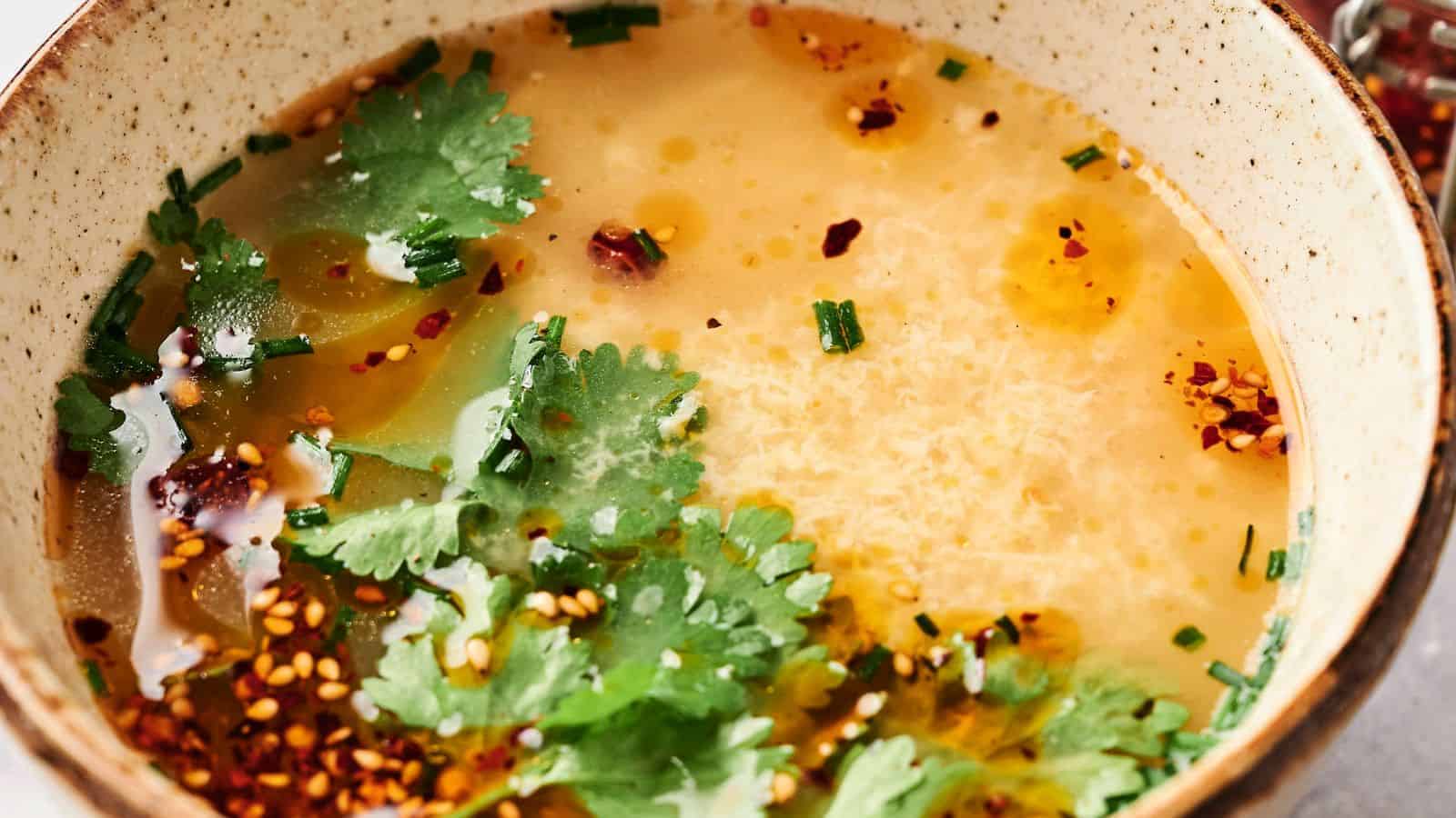 A comforting bowl of egg drop soup elegantly garnished with fresh cilantro, vibrant chives, and a sprinkle of chili flakes.